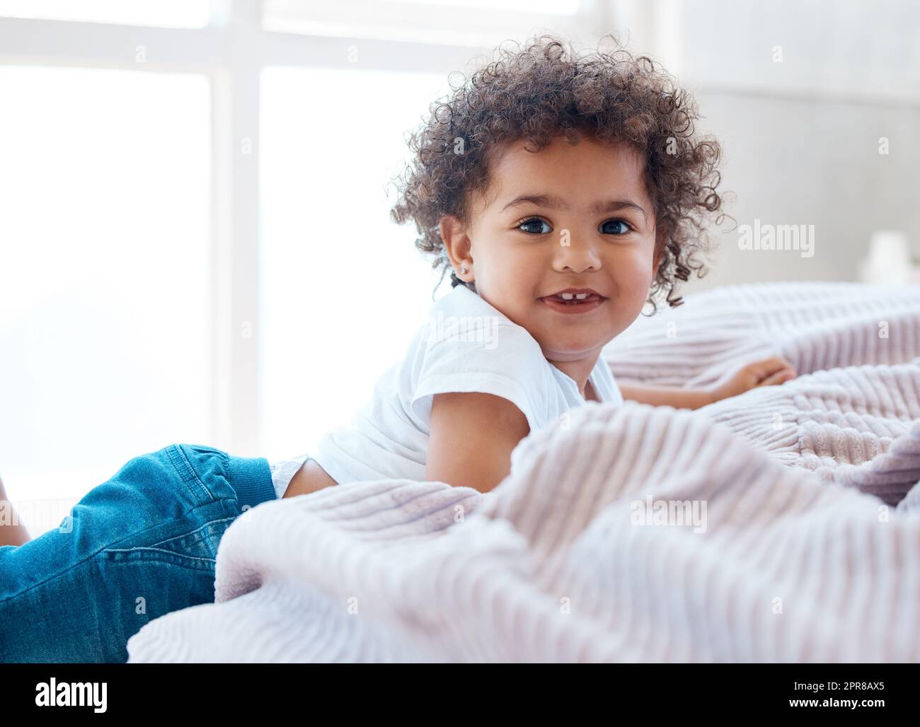 Lockige Niedlichkeitsüberlastung. Aufnahme eines entzückenden kleinen Mädchens auf einem Bett. Stockfoto