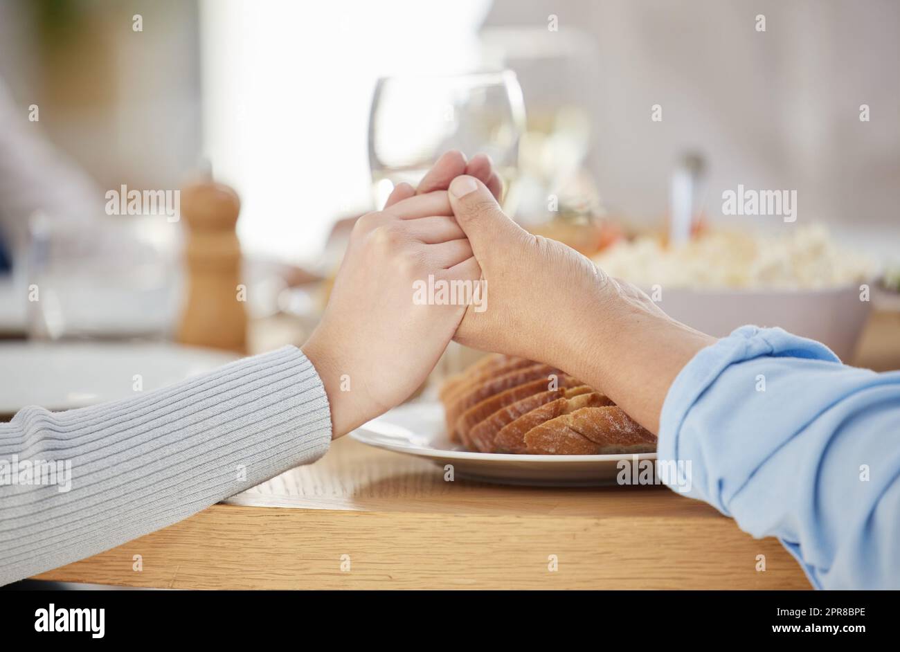 Familien, die zusammen beten, kommen zusammen in den Himmel. Zwei unkenntliche Menschen halten sich am Esstisch zu Hause die Hände. Stockfoto