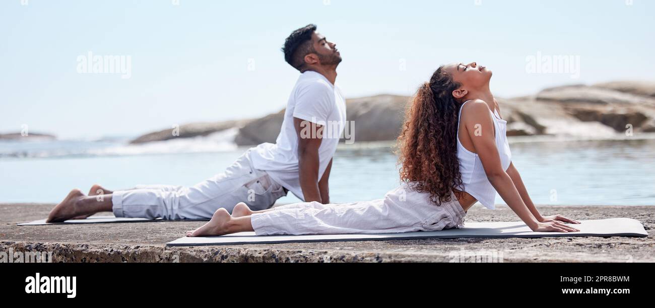 Gut für Geist, Körper und Seele. Ganzkörperaufnahme eines jungen Paares, das am Strand Yoga praktiziert. Stockfoto