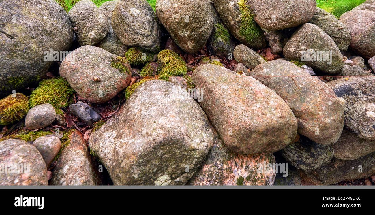 Nahaufnahme von vielen großen Felsen, bedeckt mit Flechten. Landschaft aus grünem Moos, die sich auf einem Haufen verwitterter Steine in wilder oder unkultivierter Umgebung abhebt. Wunderschöne Details rauer felsiger Naturtexturen Stockfoto