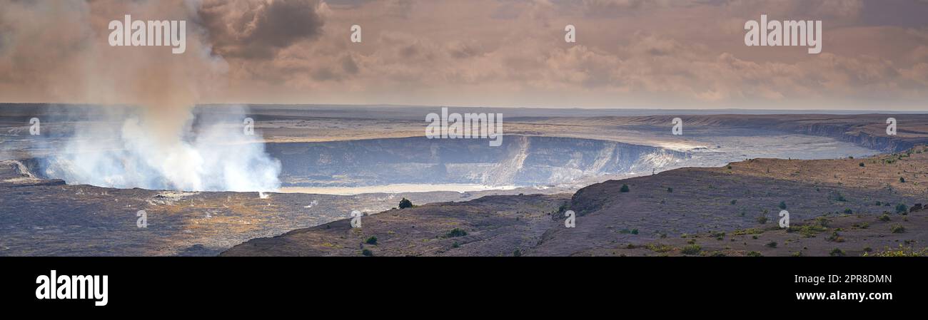 Mouna Kea der aktivste Vulkan an einem bewölkten Tag. Extreme Panoramalandschaft des hawaiianischen Berges mit grünen Feldern im Vordergrund. Der bedeckte Himmel enthüllt den kleinen dampfenden Vulkan im Hintergrund Stockfoto