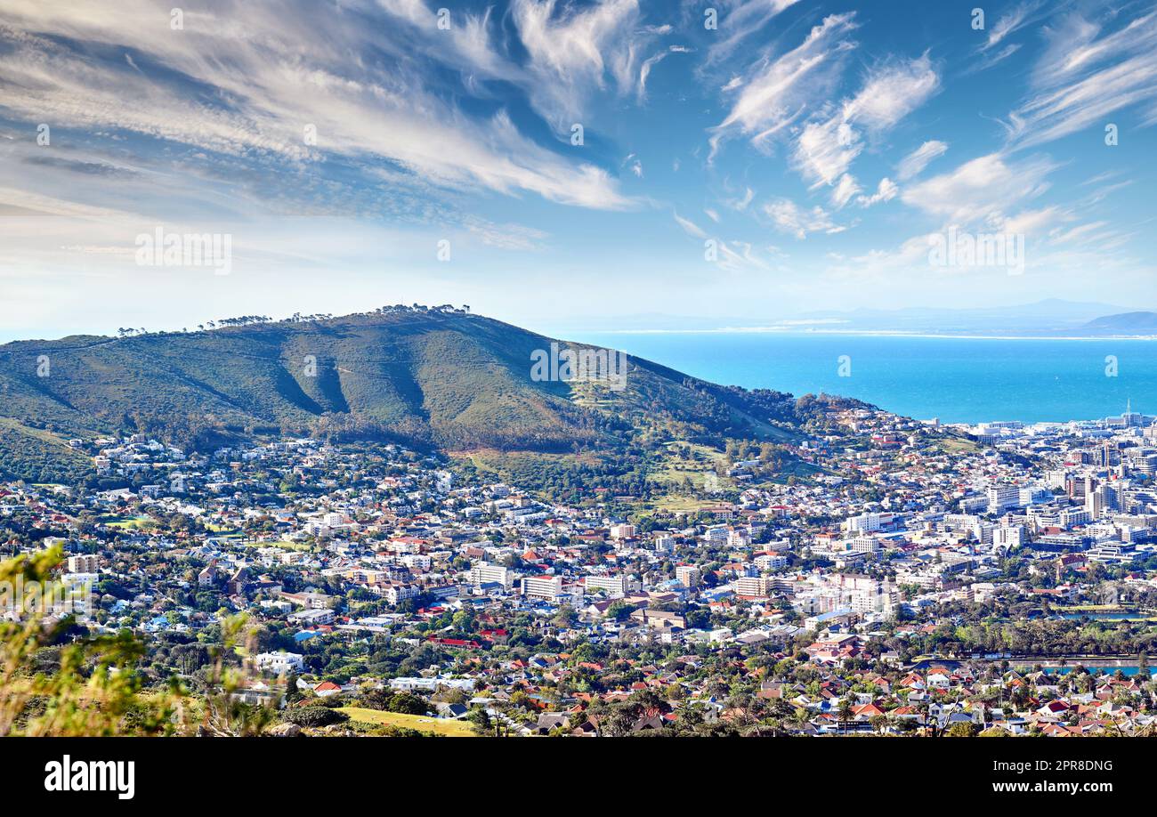 Kopieren Sie Raum mit wolkenblauem Himmel über dem Blick auf eine Küstenstadt vom Signal Hill in Kapstadt Südafrika. Malerische Panoramalandschaft von Gebäuden in einer Stadt entlang der Berge und des Meeres Stockfoto
