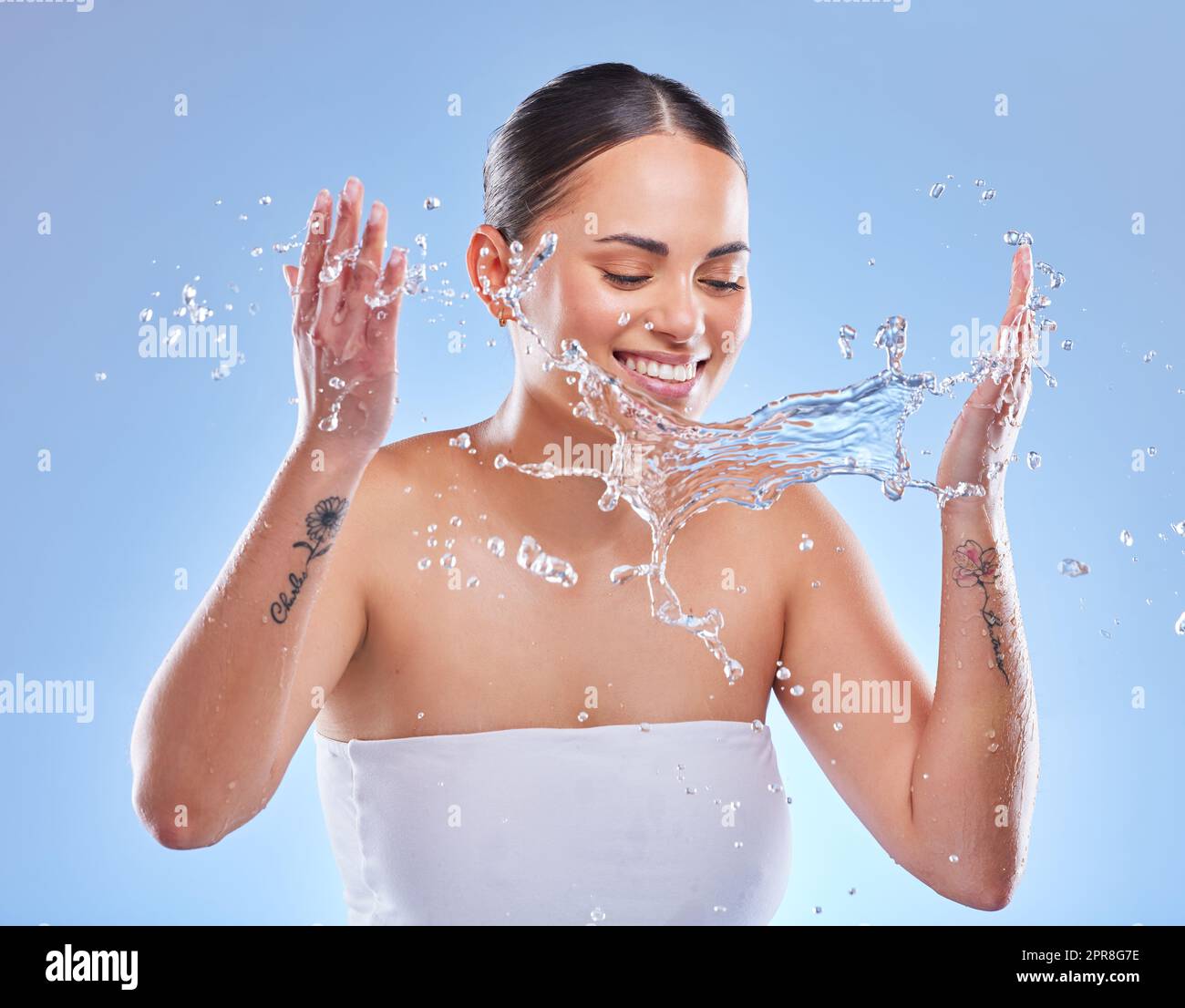 Werde nass mit mir. Aufnahme einer schönen jungen Frau, die vor blauem Hintergrund mit Wasser bespritzt wurde. Stockfoto