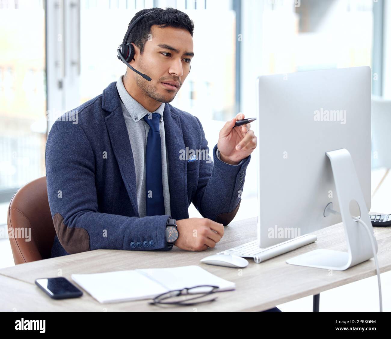 Ich verstehe, worum es geht: Ein Kundendienstmitarbeiter, der ein Headset trägt, während er an seinem Schreibtisch sitzt. Stockfoto
