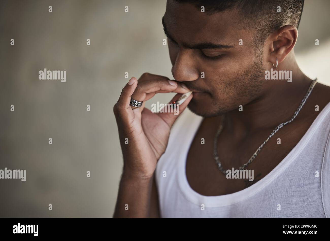 Ein junger Mann, der vor städtischem Hintergrund eine Marihuanazigarette raucht. Stockfoto