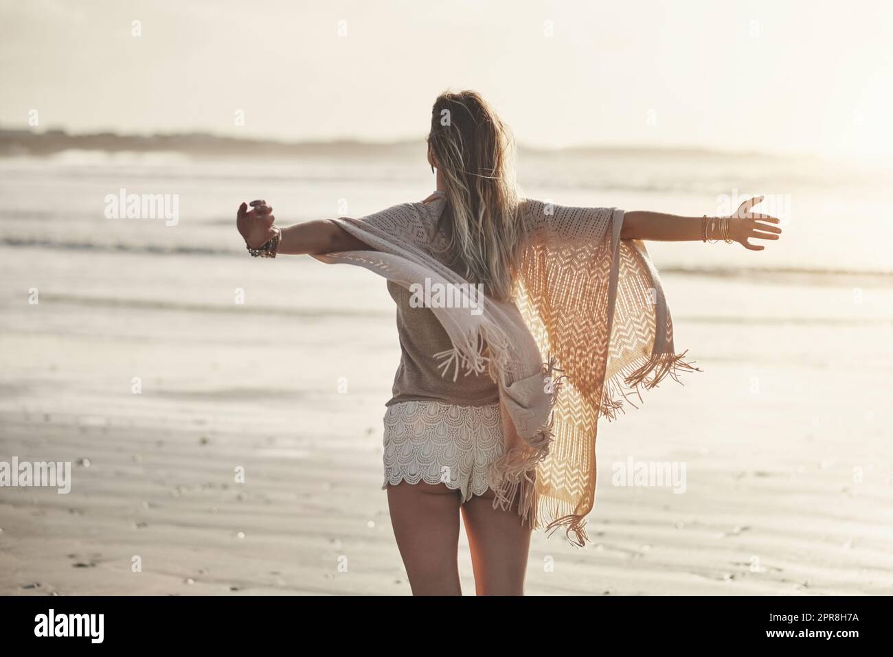 Freiheit ist hier draußen. Rückansicht einer jungen Frau, die mit ausgestreckten Armen am Strand steht. Stockfoto