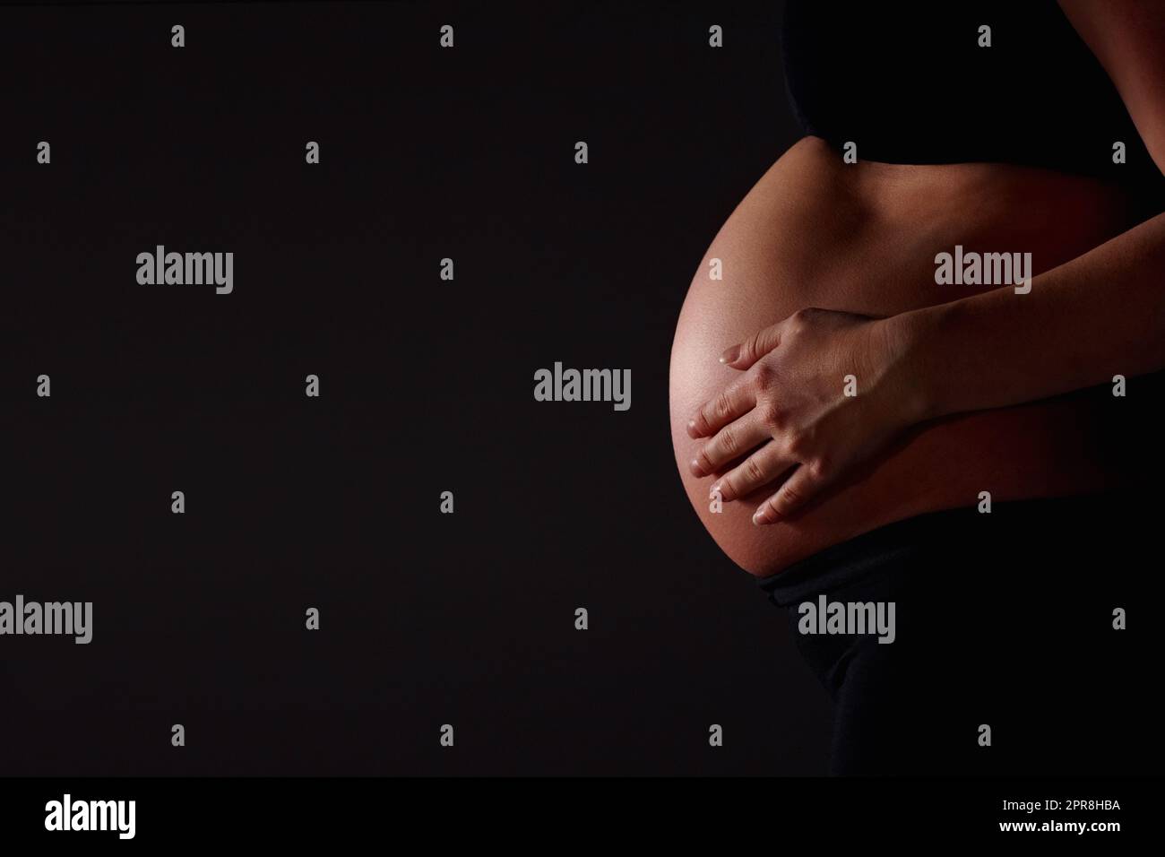 Schwanger Frau fühlt ihr Baby gegen schwarz - Copyspace. Mittelteil einer Schwangeren, die ihr Baby vor schwarzem Hintergrund fühlt - Copyspace. Stockfoto