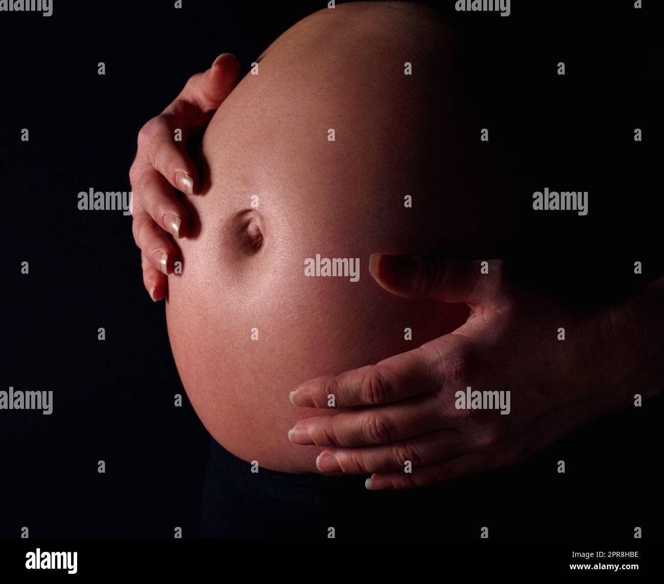 Schwanger Frau hält freiliegenden Bauch vor schwarzem Hintergrund. Detailaufnahme einer Schwangeren, die einen freiliegenden Bauch vor schwarzem Hintergrund hält. Stockfoto