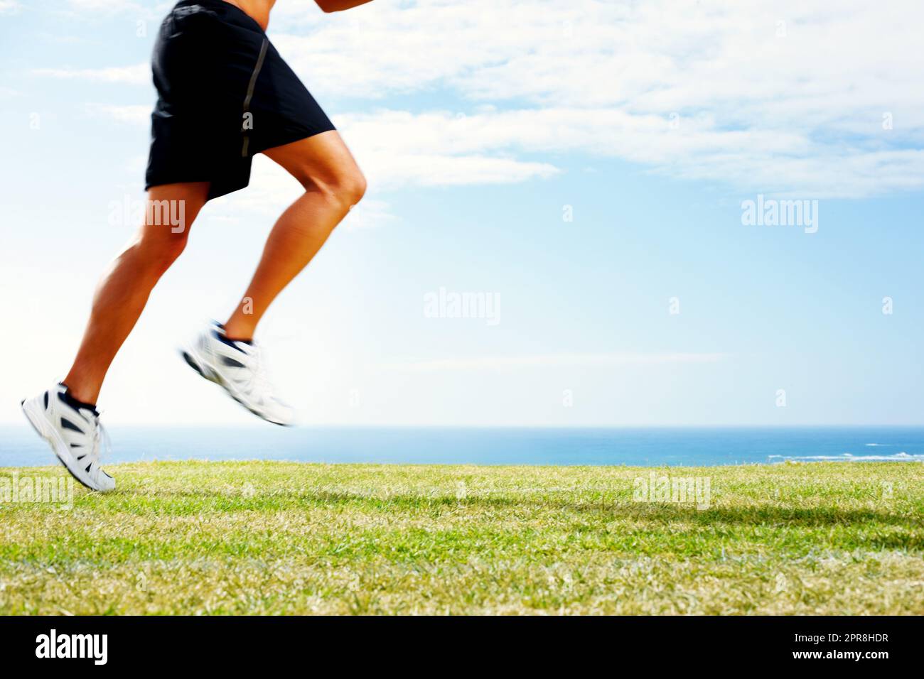 Junger Mann joggt auf dem Gras gegen den Himmel - Outdoor. Zugeschnittenes Bild eines jungen Mannes, der auf dem grünen Gras gegen den Himmel joggt. Stockfoto