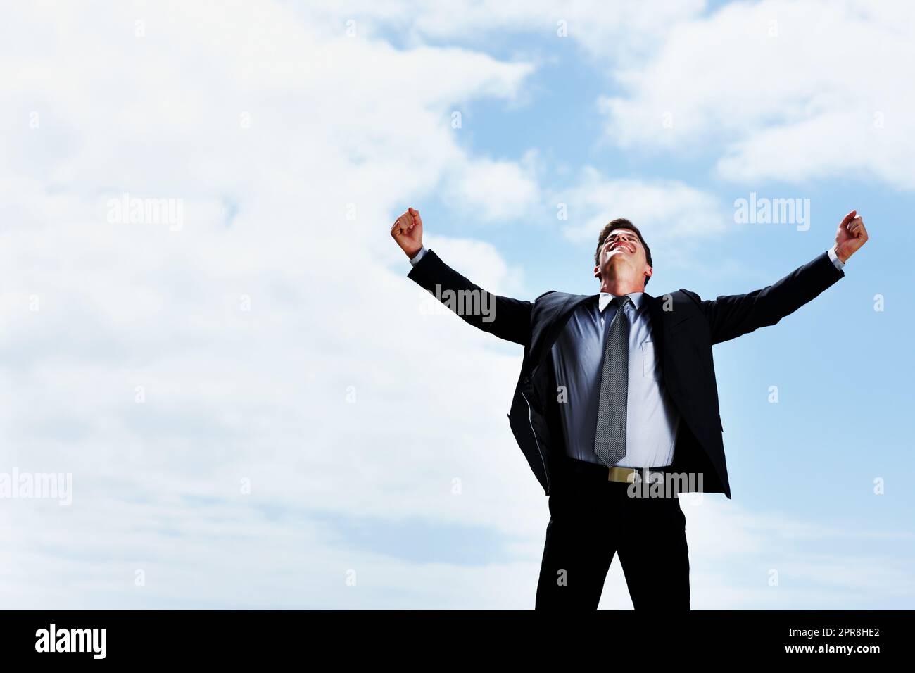 Glücklicher Geschäftsmann mit weit geöffneten Armen gegen den Himmel. Erfolgreicher Geschäftsmann mit weit geöffneten Armen und Blick zum Himmel. Stockfoto