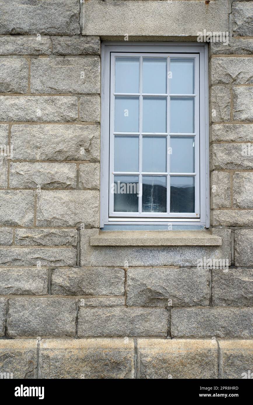Glänzendes Fenster und Architektur einer grauen Ziegelwand. Äußere Texturdetails eines alten, rustikalen Wohngebäudes oder Privathauses mit modernen Holzfenstern und Fensterbank in einer Stadt oder einem Dorf Stockfoto