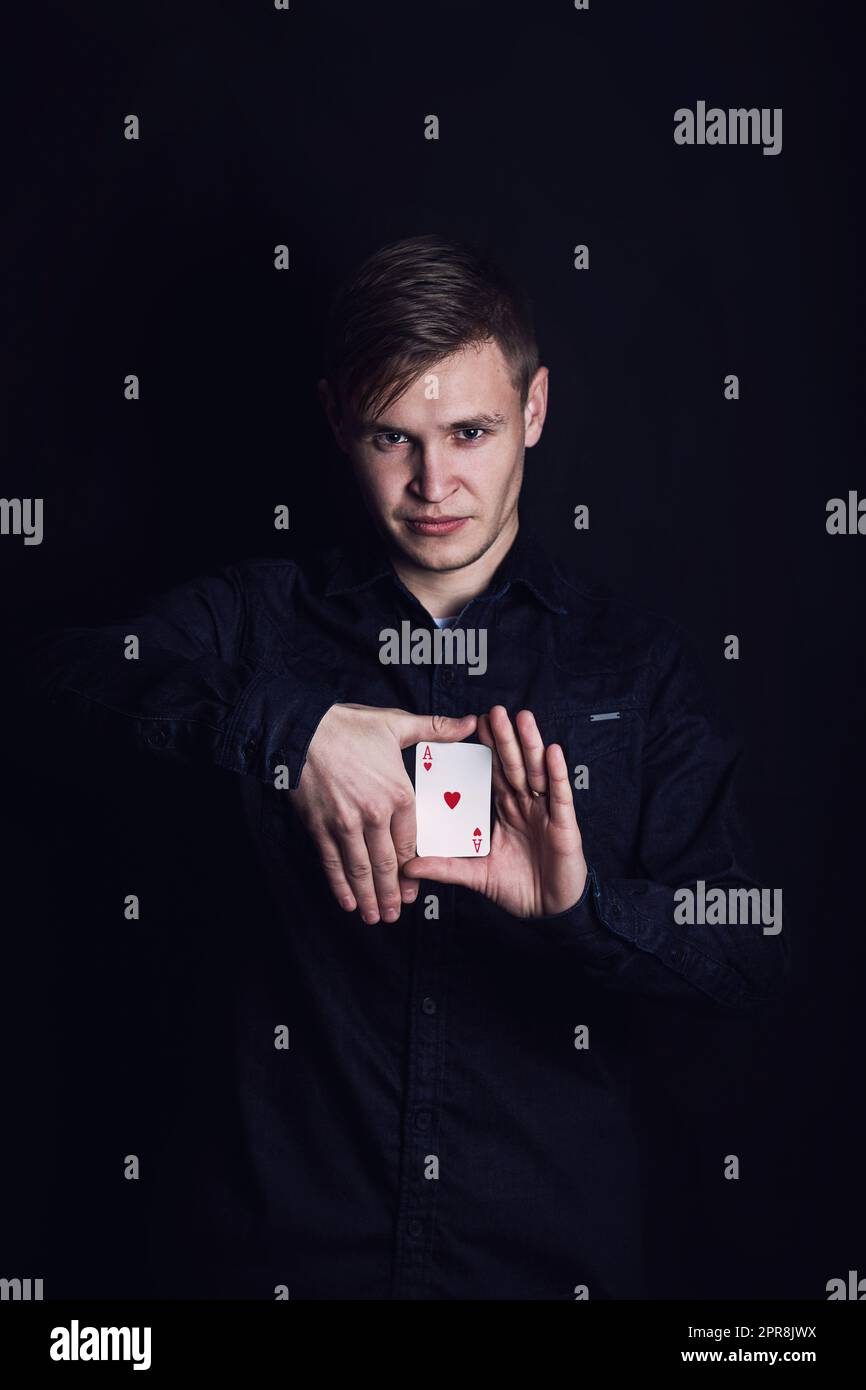 Selbstbewusster junger Mann zeigt Tricks mit Karten wie ein Zauberer, isoliert auf dunklem Hintergrund. Glücksspielsieger, erfolgreicher Spieler, der Illusionen zeigt Stockfoto