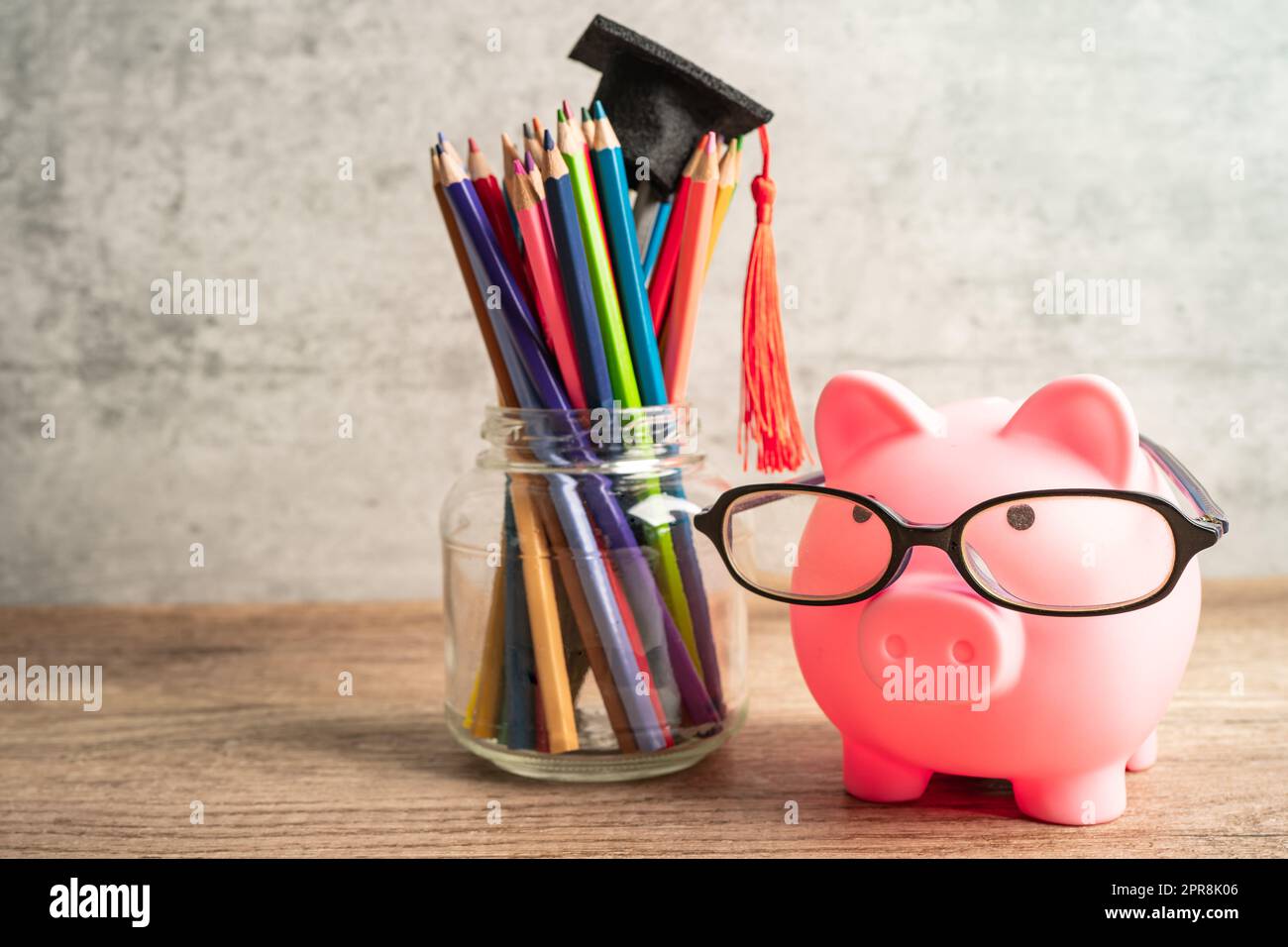 Sparschweinenbank trägt Brille mit bunten Bleistiften und spart Bankschulung. Stockfoto