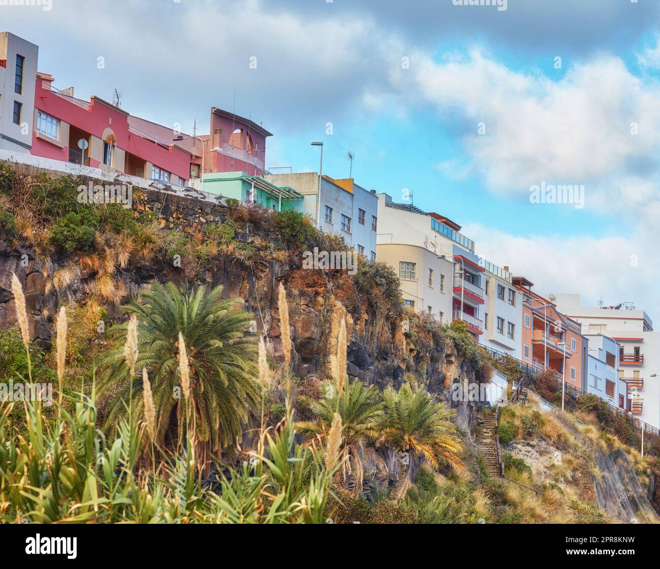 Stadtblick auf Wohnhäuser oder Gebäude auf einer Klippe in Santa Cruz, La Palma, Spanien. Historische spanische Kolonialarchitektur und Palmen im tropischen Dorf eines berühmten Reiseziels Stockfoto