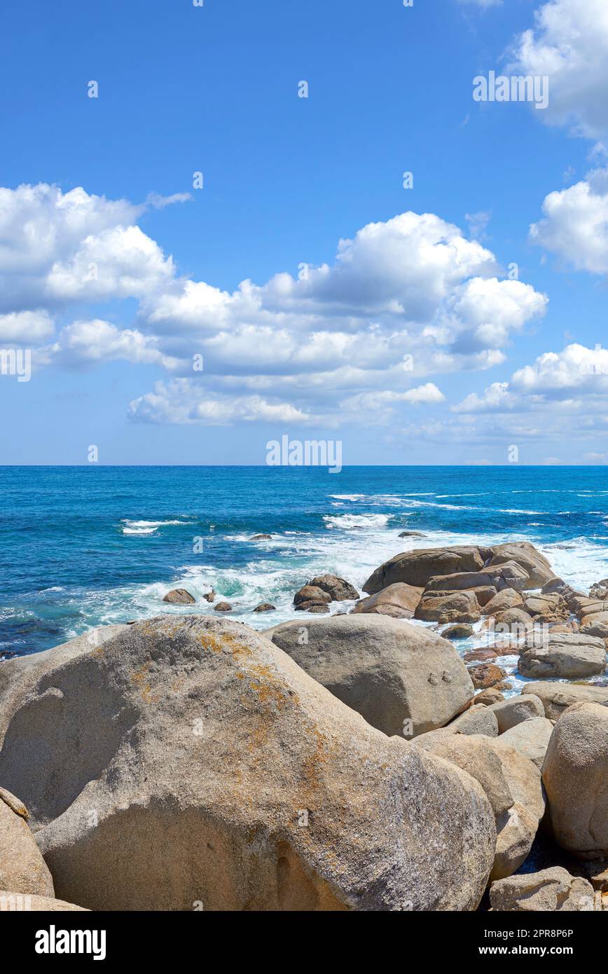 Copyspace auf dem Meer mit wolkenlosem blauem Hintergrund und felsiger Küste in Camps Bay, Kapstadt, Südafrika. Felsbrocken an einem Strandufer über einem majestätischen Ozean. Malerische Landschaft für einen Sommerurlaub Stockfoto