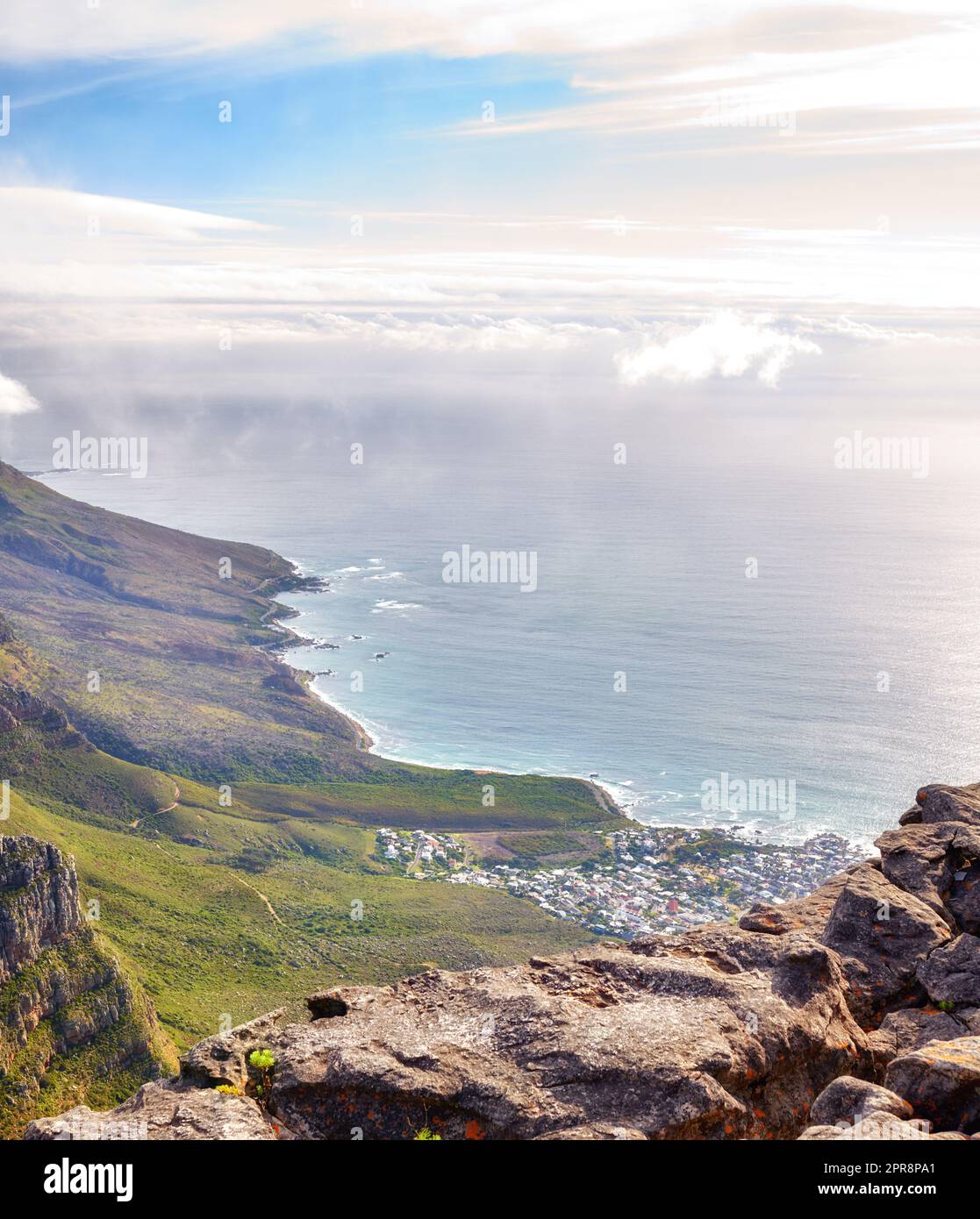 Landschaft des Lions Head Berges mit Häusern, Ozean und bewölktem Himmel mit Kopierraum. Ausblick auf grüne Berge mit viel Vegetation und Blick auf eine Stadt in Kapstadt, Südafrika Stockfoto