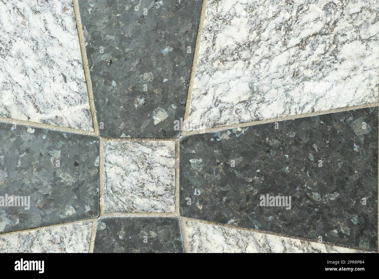 Nahaufnahme von schwarzen und grauen Granitfliesen auf einem Boden. Kreatives Architekturdesign aus Granitfliesen, die zu einem Kreuzmuster zementiert sind. Texturhintergrund aus Naturstein für Innendesign Stockfoto