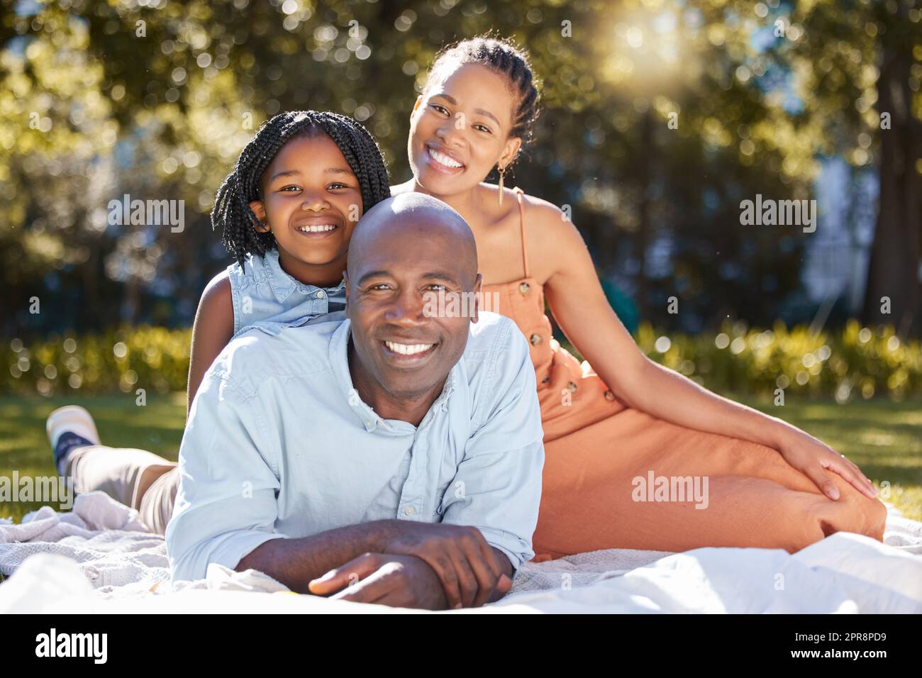 Portrait glückliche afroamerikanische Familie mit drei Personen, die im Sommer eine schöne Zeit zusammen im Park verbringen. Mutter, Vater und Tochter, die sich draußen anfreunden. Ein süßes Mädchen und Eltern, die draußen lächeln Stockfoto