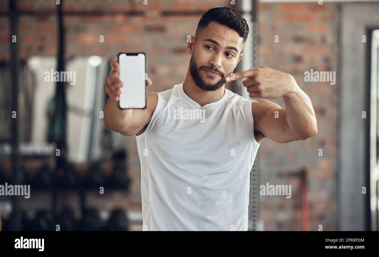 Ein Athlet, der einen Gesichtsausdruck mit seinem Handy macht. Fit, junger Mann, der sein Mobilgerät im Fitnessstudio zeigt. Ein hübscher junger Mann, der sein Handy im Fitnessstudio benutzt. Bodybuilder zeigt auf sein Handy Stockfoto