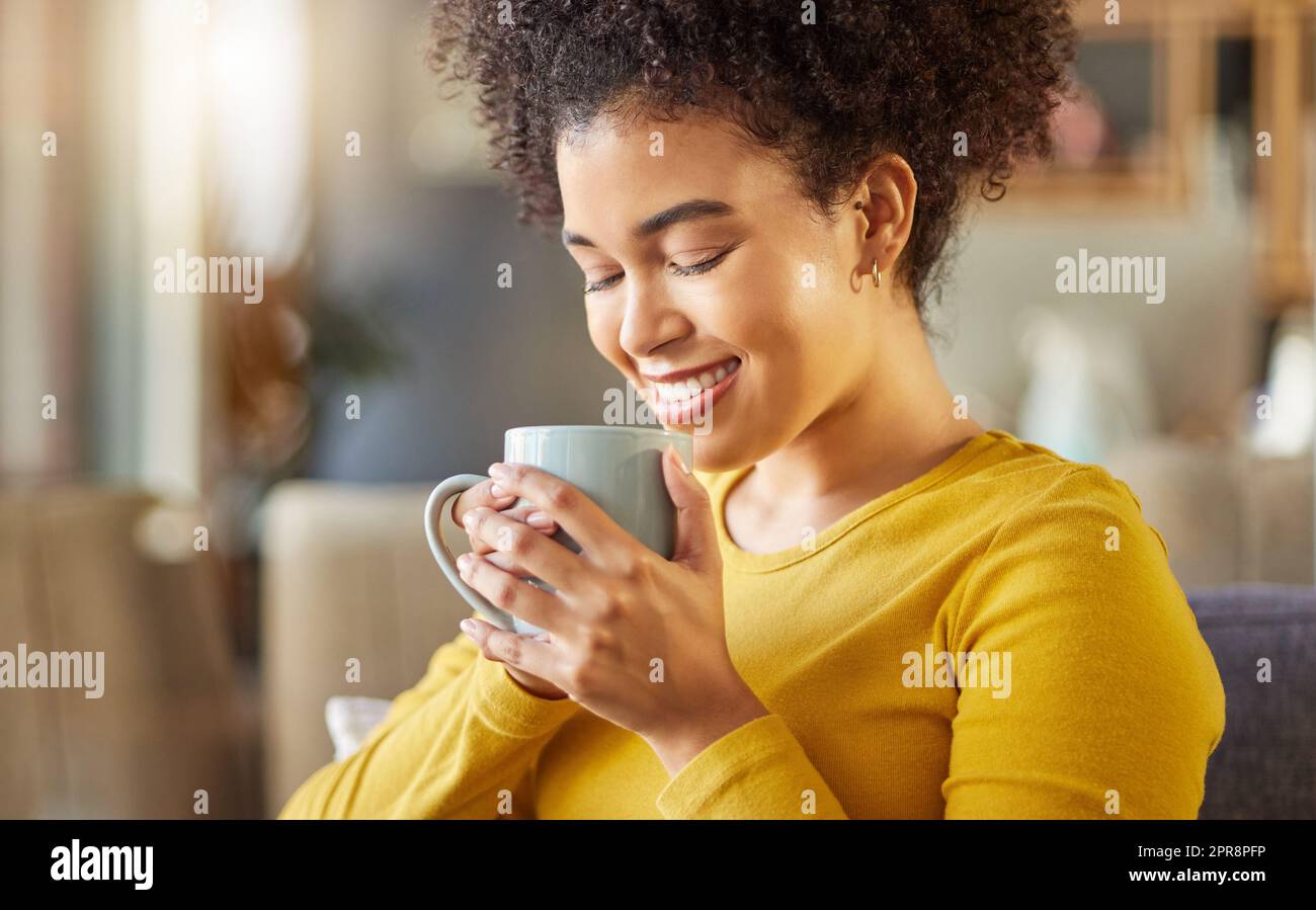 Junge glückliche Mischrasse Frau, die zu Hause eine Tasse Kaffee hält und trinkt. Eine gemütliche hispanische Frau lächelt und genießt eine Tasse Tee, während Sie sich zu Hause entspannen Stockfoto