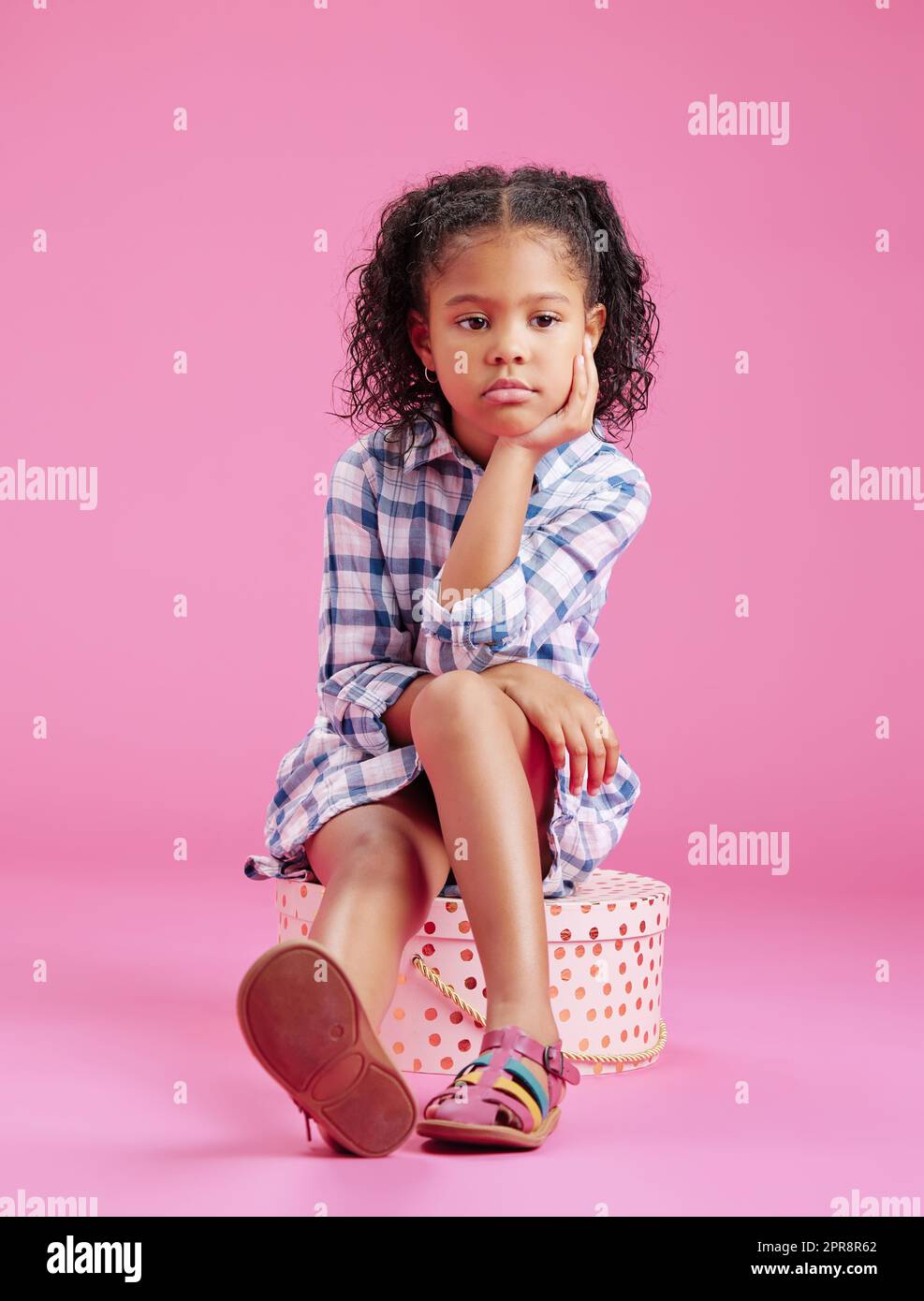 Ein süßes, gemischtes Mädchen sitzt in einem Studio und träumt vor einem pinkfarbenen Hintergrund. Ein einsames afroamerikanisches Kind, das traurig und deprimiert aussieht Stockfoto