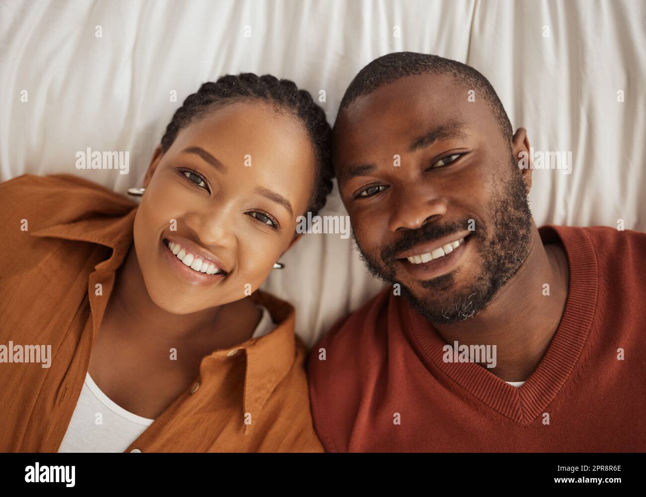 Porträt eines liebenden afroamerikaners, der von oben auf einem Bett zusammenliegt. Glücklicher junger Mann und Frau lächeln und blicken in die Kamera Stockfoto