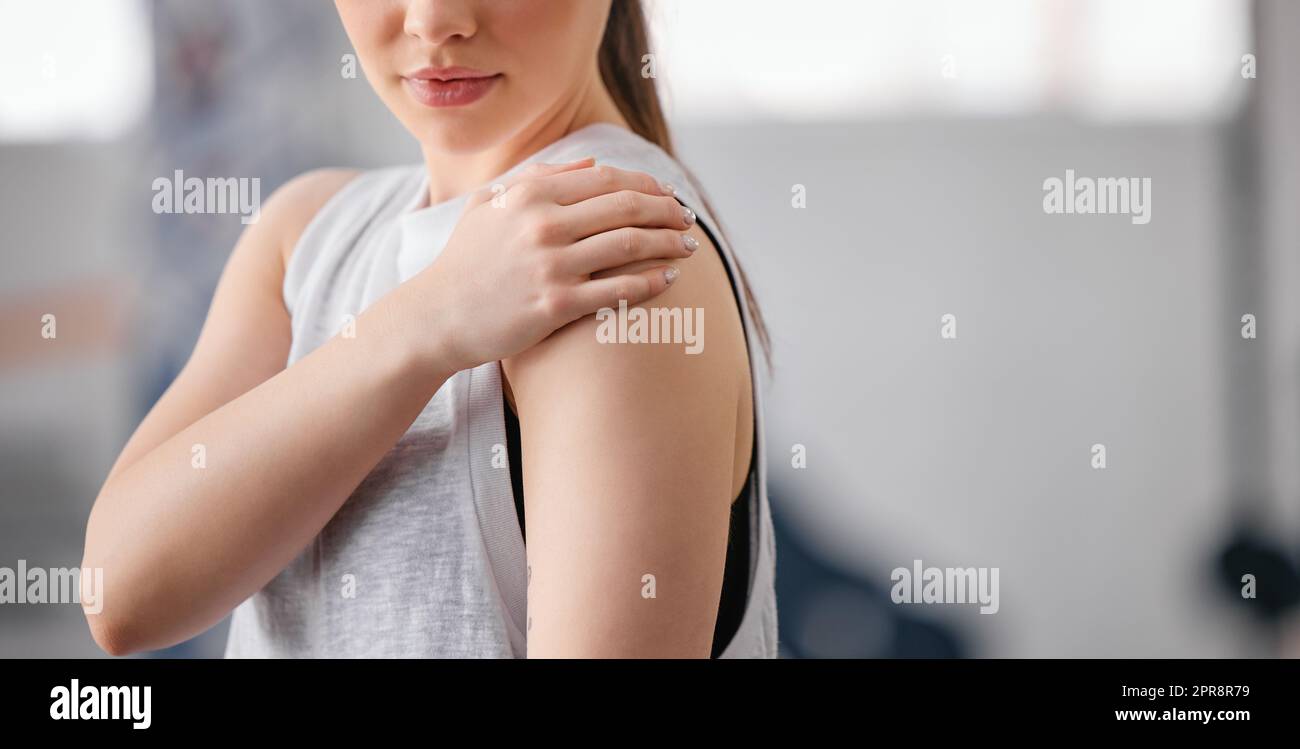 Nahaufnahme einer weißhäutigen Frau, die beim Training in einem Fitnessstudio ihre schmerzende Schulter hielt. Sportlerin mit schmerzhafter Armverletzung durch Gelenkfraktur und Muskelentzündung während des Trainings. Schwierigkeiten mit steifen Krämpfen, die Unbehagen und Belastungen verursachen Stockfoto