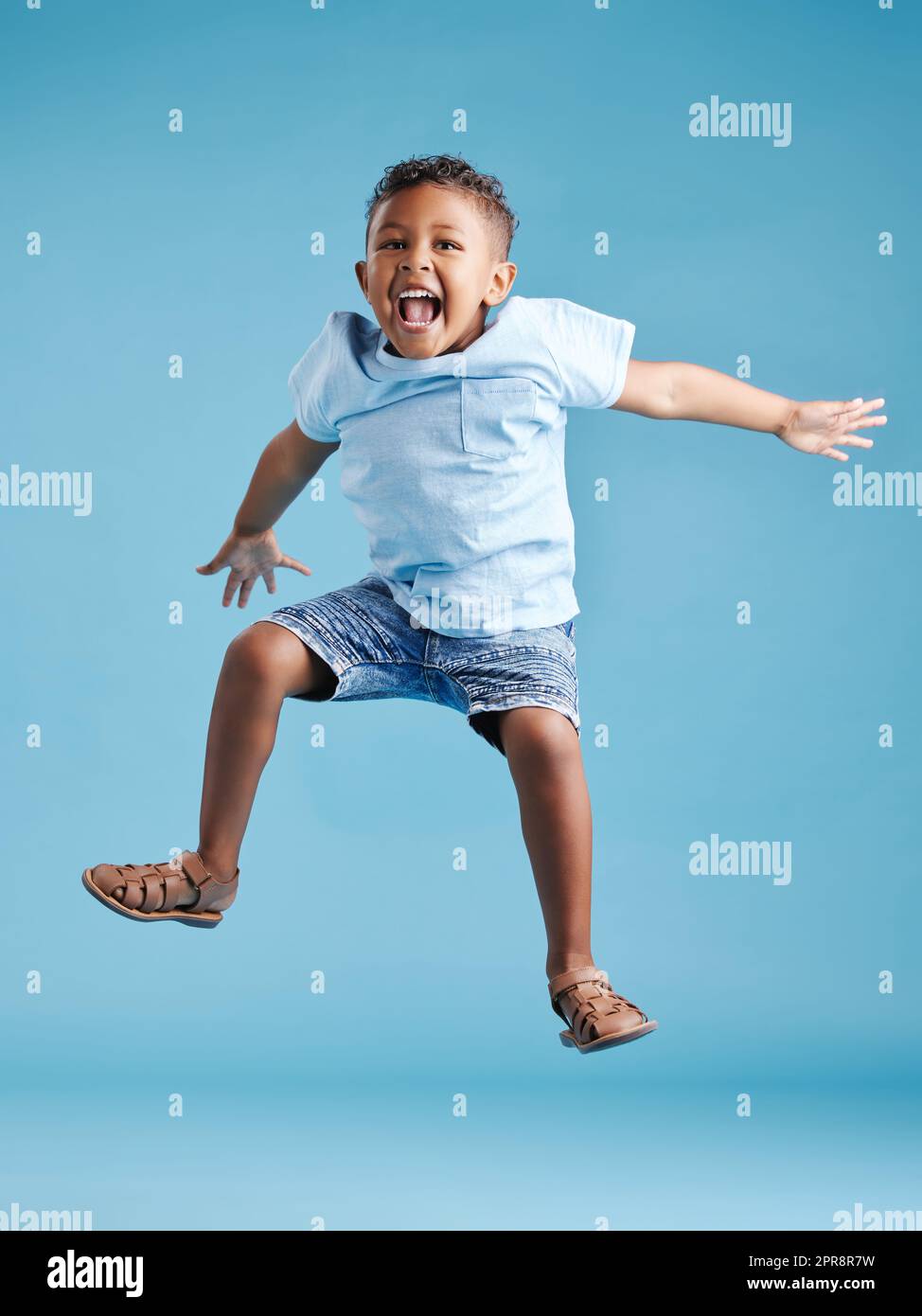 Fröhlicher junger, bezaubernder kleiner lateinamerikanischer Junge, der in die Luft springt, isoliert auf blauem Hintergrund. Lustiger Vorschulkinder, der seine Aufregung ausdrückt und Spaß hat Stockfoto