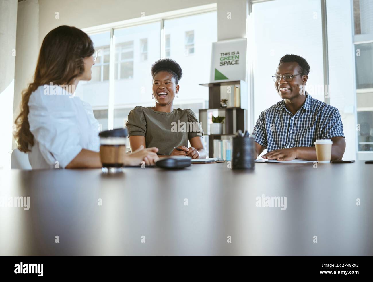 Drei junge, glückliche Geschäftsleute, die ein Meeting haben, während sie an einem Tisch bei der Arbeit sitzen. Fröhliche Geschäftsleute, die gemeinsam in einem Büro sprechen und planen Stockfoto