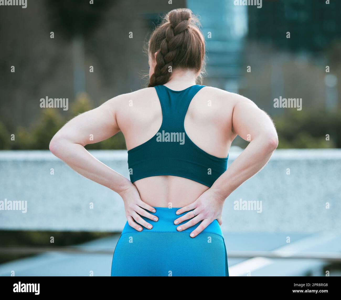 Eine weiße Frau von hinten hält Wunde Rückenpartie, während sie draußen trainiert. Sportlerin mit schmerzhafter Wirbelsäulenverletzung durch Gelenkfraktur und Muskelentzündung während des Trainings. Schwierigkeiten mit steifen Krämpfen, die Unbehagen und Belastungen verursachen Stockfoto