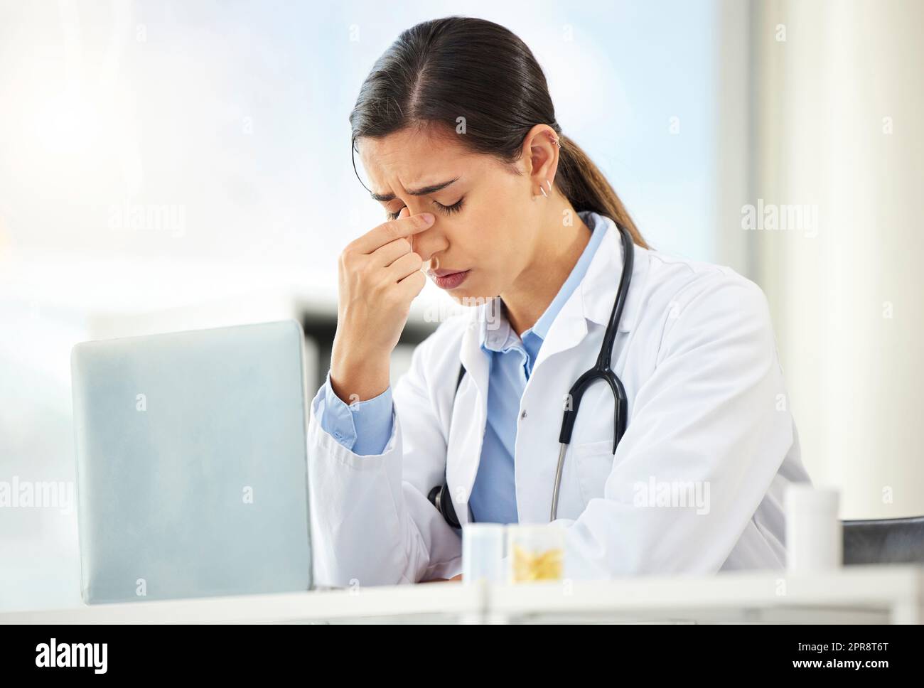 Nahaufnahme einer jungen gemischten Ärztin, die besorgt aussah und Kopfschmerzen hatte, während sie an einem Computer in ihrem Büro arbeitete. Hispanische Frau mit Kopfschmerzen und Stress im Krankenhaus Stockfoto
