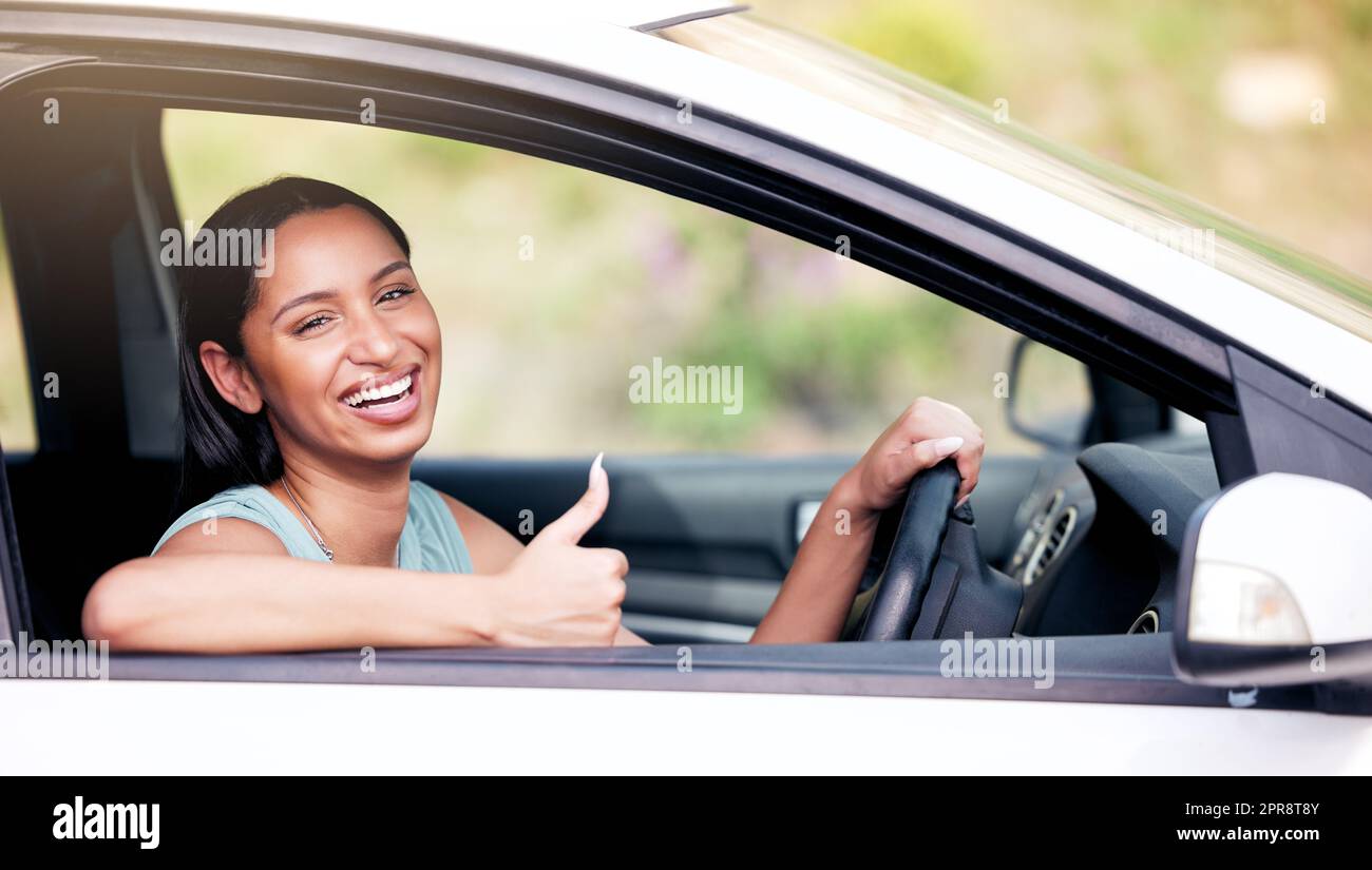 Fröhliche Mischlingsfrau, die beim Fahren ihres neuen Wagens Daumen nach oben zeigt. Frau, die glücklich aussieht, nachdem sie ihr erstes Auto gekauft hat oder nachdem sie ihre Führerscheinprüfung bestanden hat. Autoversicherung Stockfoto