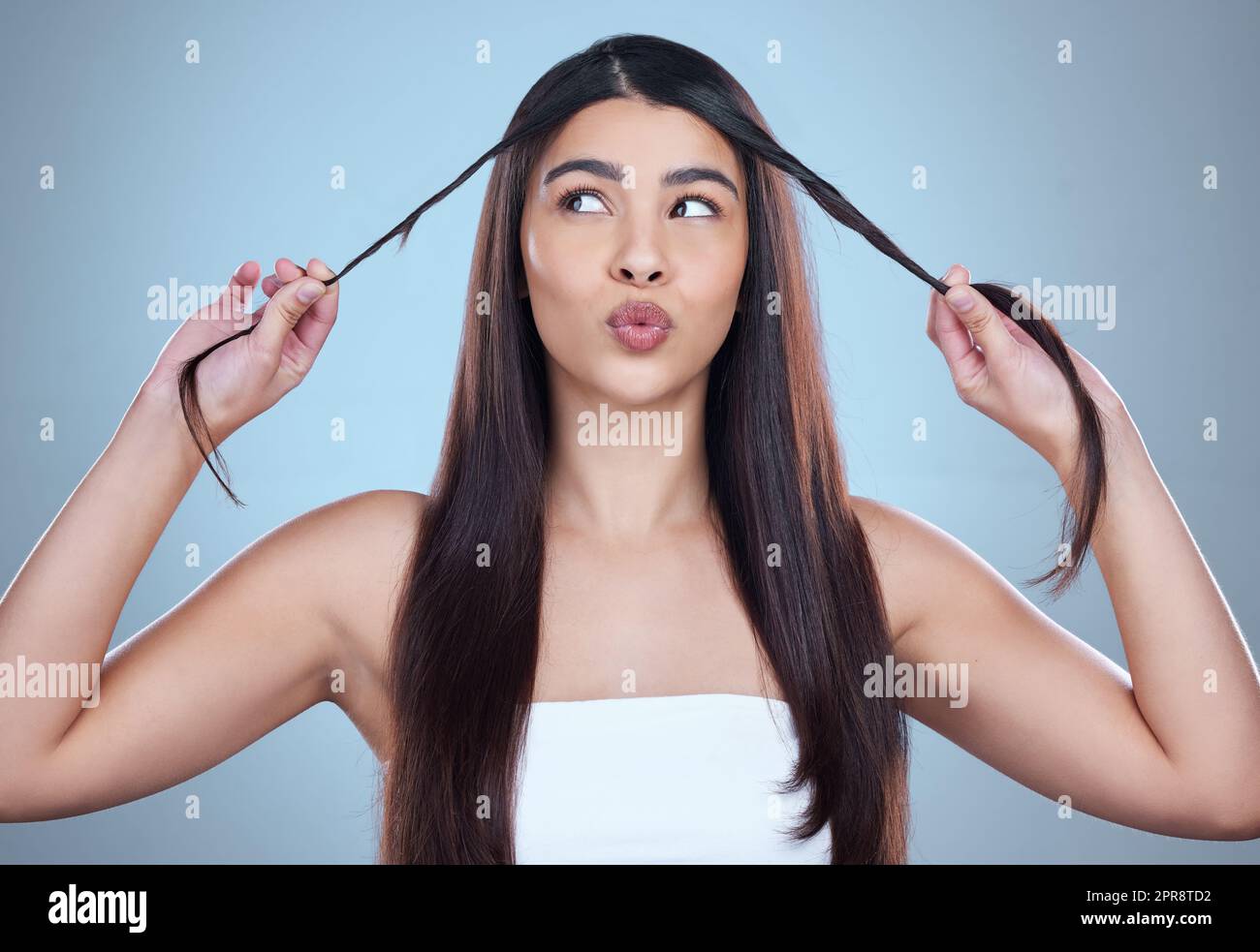 Nach oben oder unten. Studioaufnahme einer schönen jungen Frau, die ihr langes seidiges Haar vor blauem Hintergrund zeigt. Stockfoto