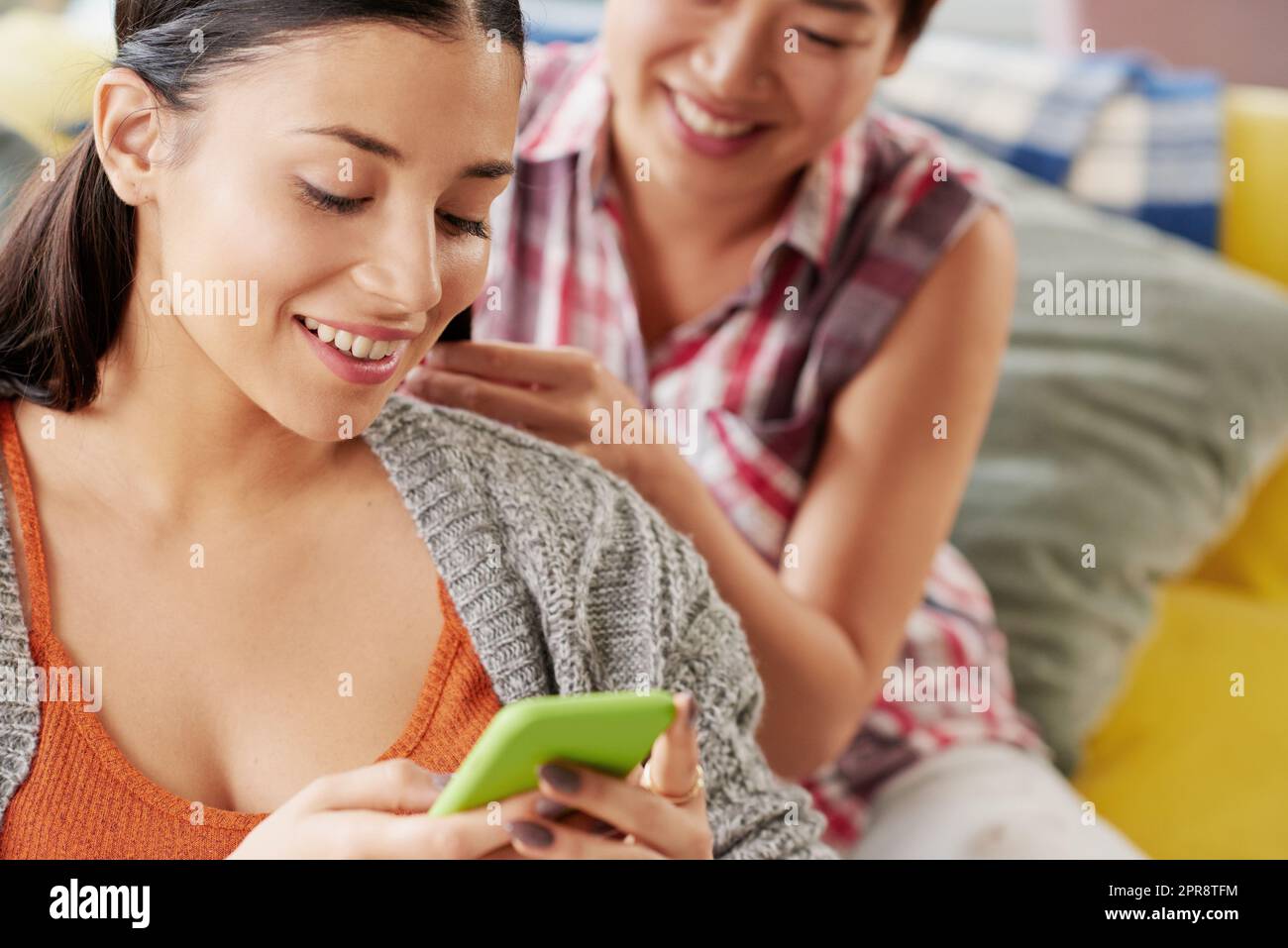 Sehen Sie sich diesen Text an. Eine Frau, die auf ihrem Handy etwas ansieht, während ihre Freundin ihre Haare macht. Stockfoto
