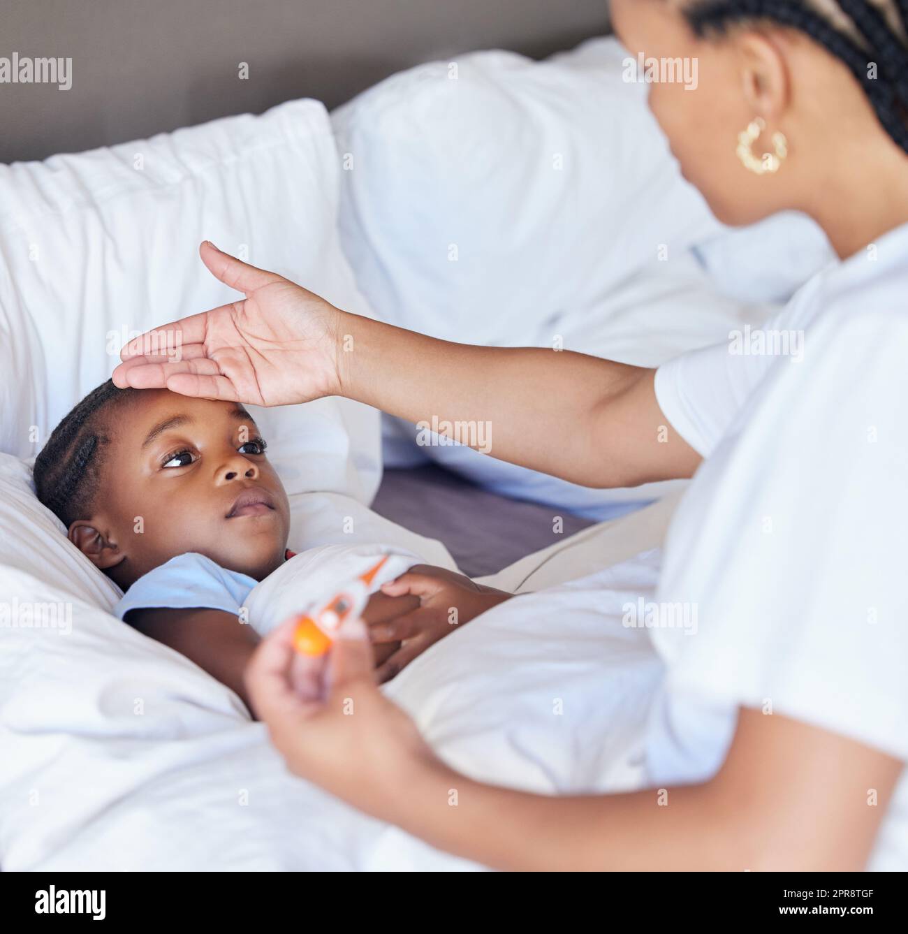 Krankes kleines Mädchen im Bett, während ihre Mutter ein Thermometer benutzt, um ihre Temperatur zu messen. Schwarze, alleinerziehende Tochter Stirn. Ein afroamerikanisches Kind fühlt sich krank, während seine Mutter Fieber untersucht Stockfoto