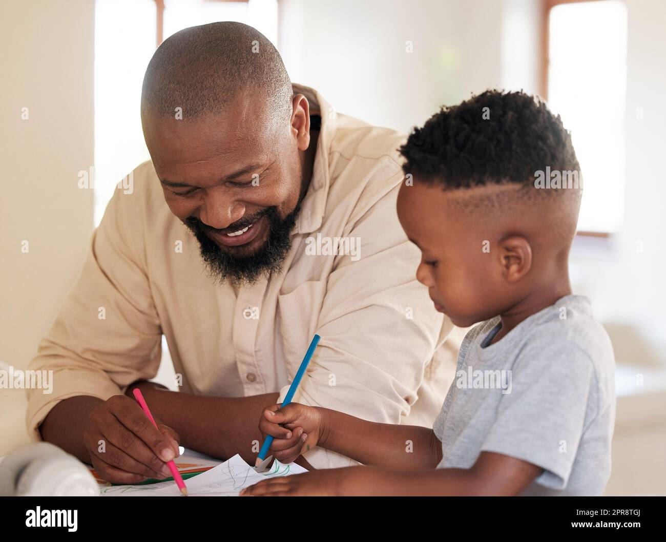 Ein afroamerikanischer Junge macht Hausaufgaben mit seinem Vater. Ein gutaussehender Schwarzer, der seinem Sohn bei der Schularbeit zu Hause hilft. Es ist wichtig, zu lernen und eine Ausbildung zu erhalten. Ein über- und untergeordnetes Element, das an einem Projekt arbeitet Stockfoto