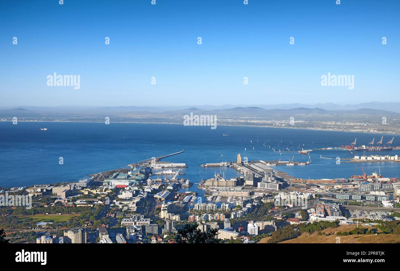 Luftaufnahme einer Stadt und des Ozeans mit Hafen in Kapstadt während des Tages. Malerischer Landschaftsblick auf einen kleinen Hafen, städtische Gebäude und Meereslandschaft vor blauem Himmel mit Kopierraum in Südafrika Stockfoto