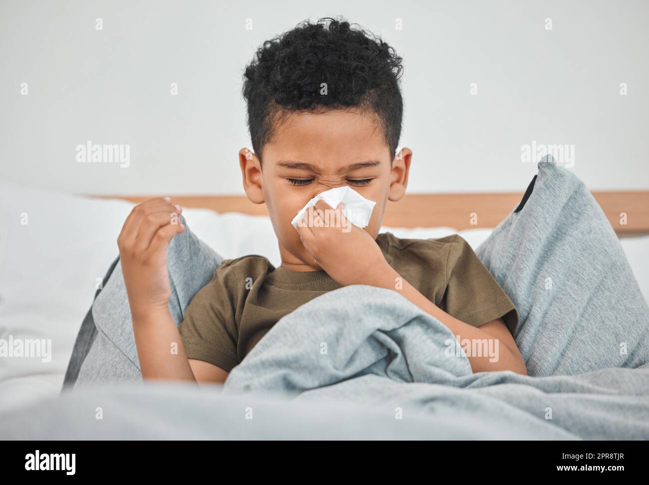 Ein kleiner Junge bläst seine Nase, während er im Bett eines Hauses war. Stockfoto