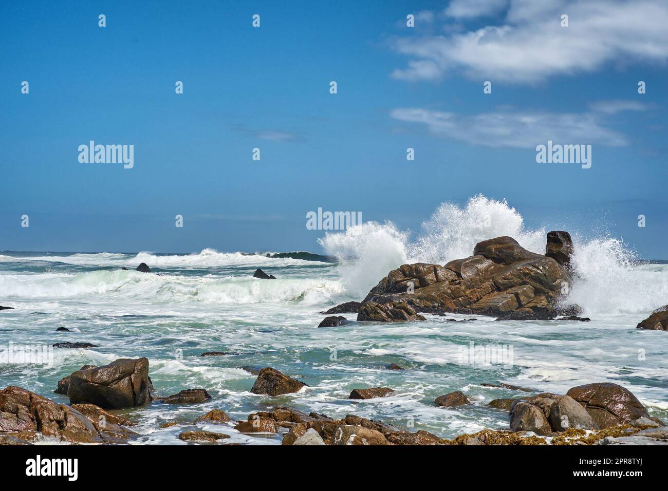 Große Wellen, die an der Küste planschen und brechen. Turbulentes Meer mit rauen Gezeiten durch starke Winde, die auf Strandfelsen mit blauem Himmelshintergrund aufprallen. Felsenküste in Camps Bay, Südafrika Stockfoto