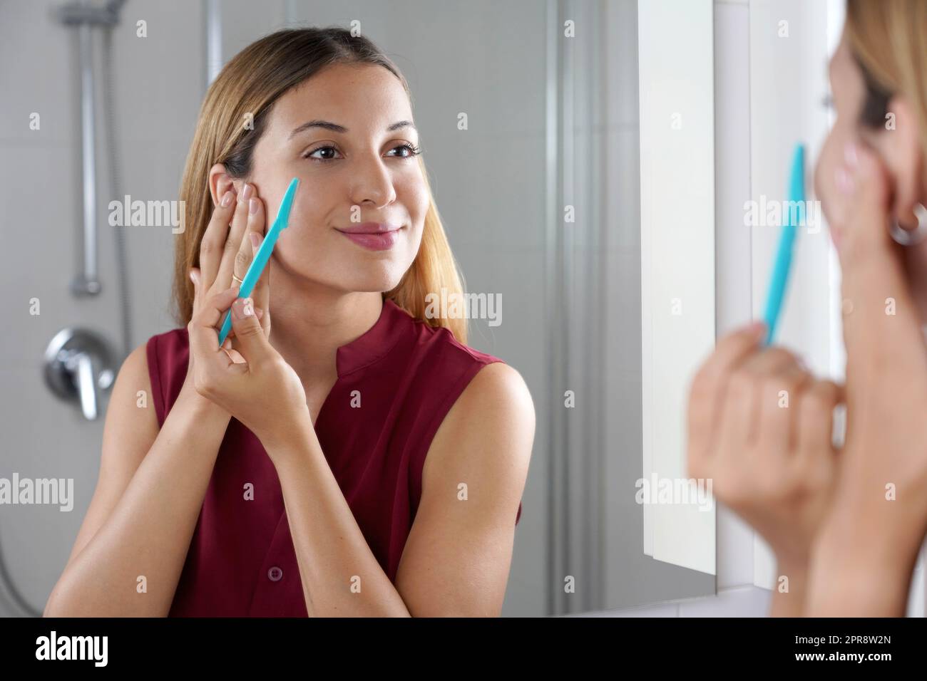 Entfernung von Gesichtshaaren. Brasilianisches Mädchen, das sich zu Hause mit einem Rasiermesser ins Gesicht rasiert. Schöne junge Frau mit Rasiermesser auf Bad. Stockfoto