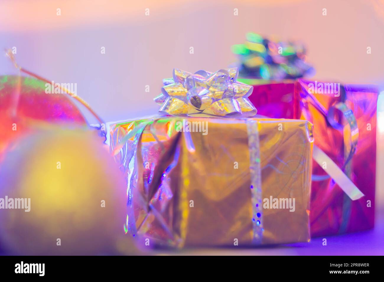 Silvester-Geschenk in einem hellen Paket vor dem Hintergrund von Weihnachtsdekorationen und hellen Lichtern der Girlande. Stockfoto