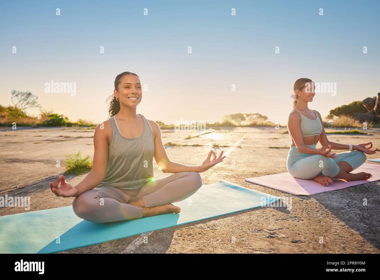 Lange Yoga-Frauen meditieren mit gekreuzten Beinen für Outdoor-Übungen in abgelegener Natur. Gemischte Rasse und kaukasische aktive Menschen, die sich für die psychische Gesundheit verbinden und ausbalancieren. Jung, gelassen und Zen Stockfoto