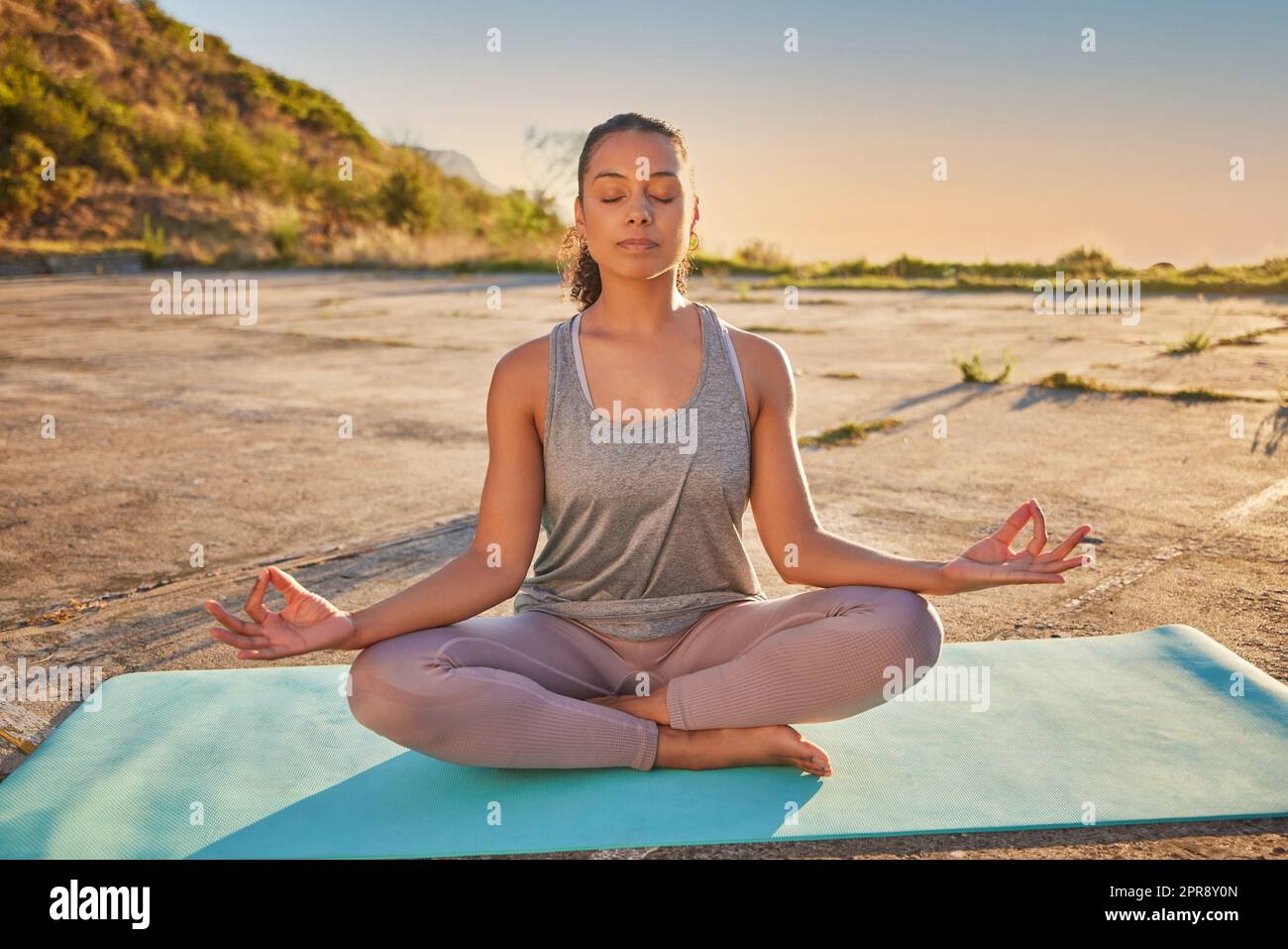 Lange Yoga-Frau meditiert mit gekreuzten Beinen für Outdoor-Training in abgelegener Natur. Gemischtrassenorientierte aktive Person, die allein sitzt und für die psychische Gesundheit balanciert. Junge hispanische Ruhe und Zen Stockfoto
