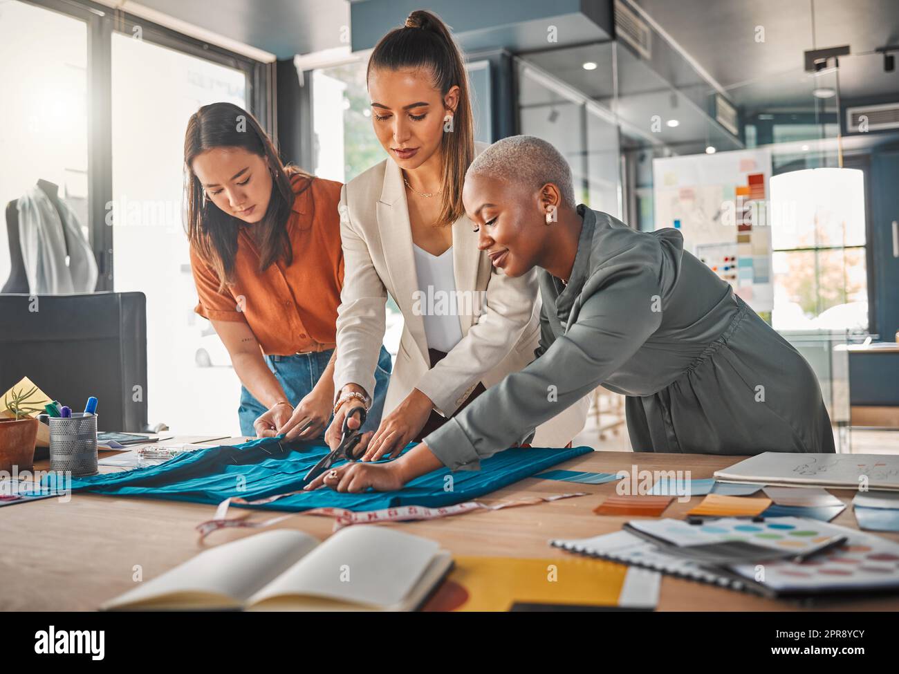 Alle arbeiten, um zum Erfolg zu kommen. Eine Gruppe junger Designerinnen schneidet Material in einer Boutique. Stockfoto