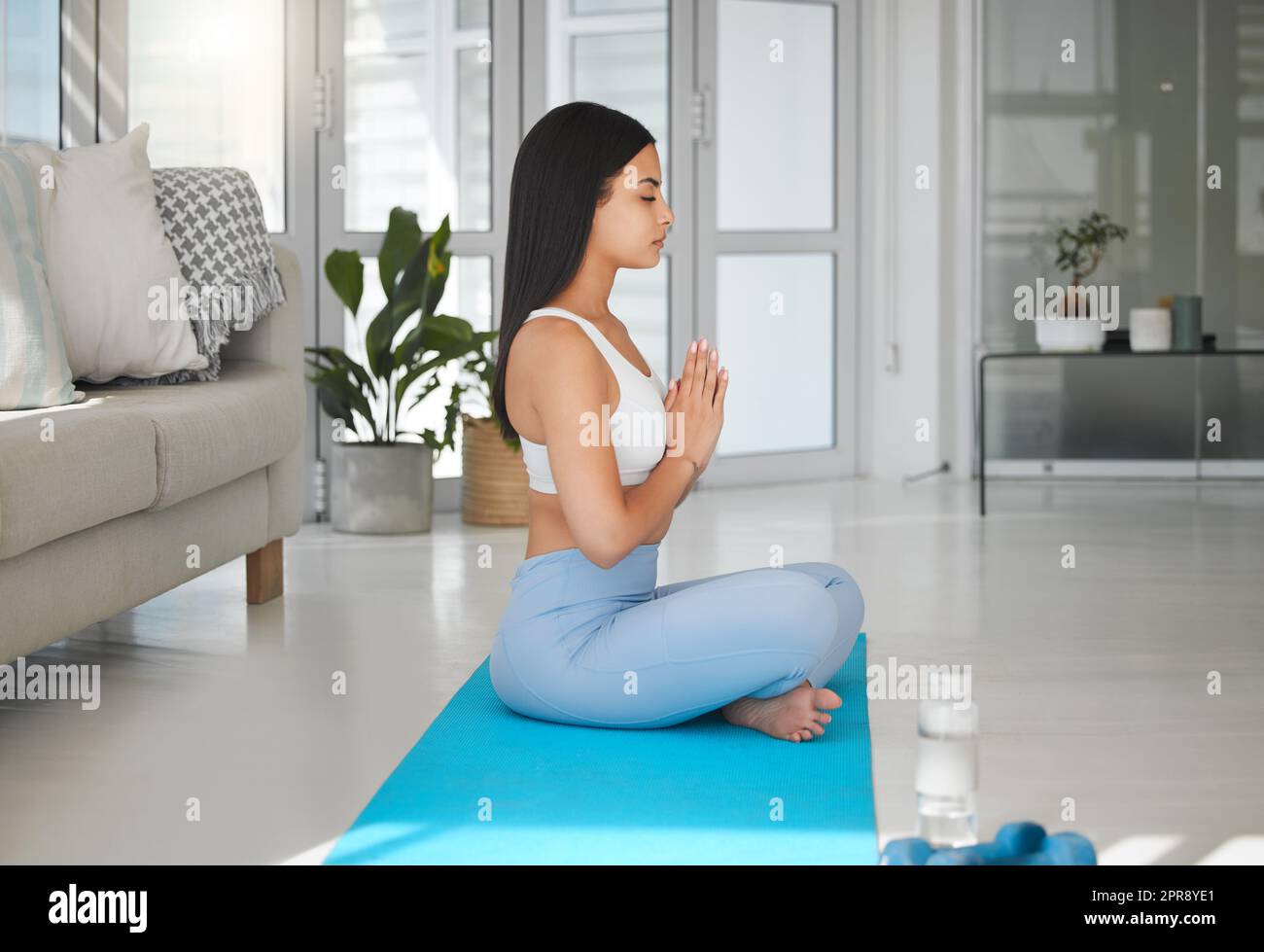 Treiben Sie sich geistig, körperlich und geistig an. Eine sportliche junge Frau meditiert während sie zu Hause Yoga praktiziert. Stockfoto