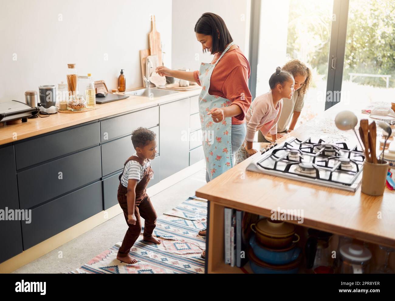 Eine glückliche Mischrasse aus fünf Personen, die zusammen kochen und Spaß in einer Küche haben. Liebe schwarze alleinerziehende Eltern, die sich mit ihren Kindern verbinden und ihnen häusliche Fähigkeiten zu Hause beibringen Stockfoto