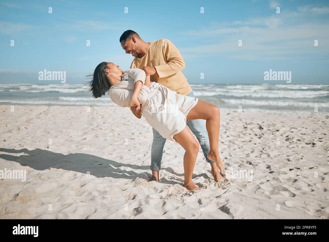 Liebevolles junges gemischtes Paar, das am Strand tanzt. Glücklicher junger Mann und verliebte Frau genießen romantische Momente während der Flitterwochen am Meer Stockfoto