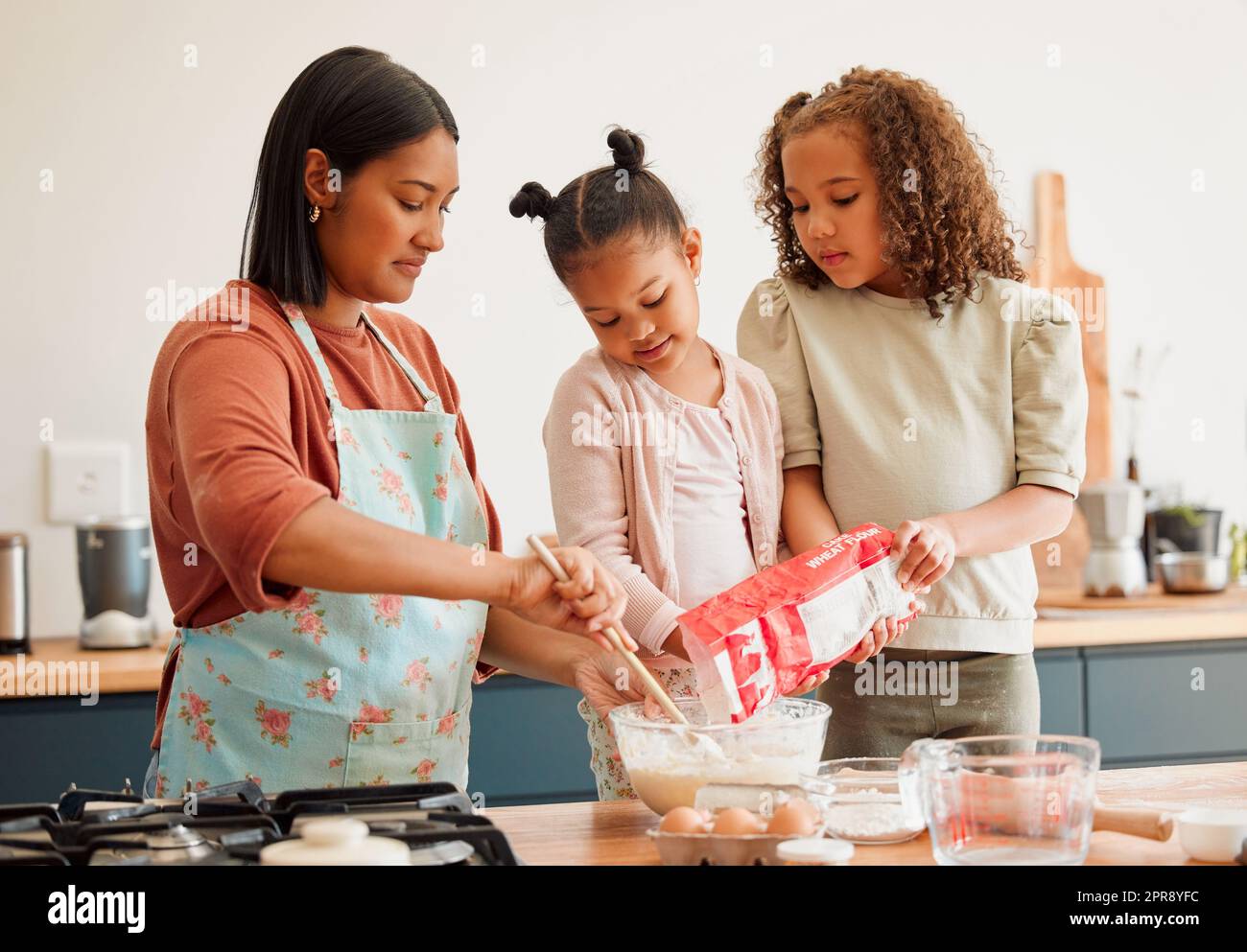 Nur Frauen, glücklich gemischte Rasse Familie von drei Kochen in einer chaotischen Küche zusammen. Liebevolle schwarze alleinerziehende Mutter, die sich während der Lehrei mit ihren Töchtern zusammenhängt Stockfoto