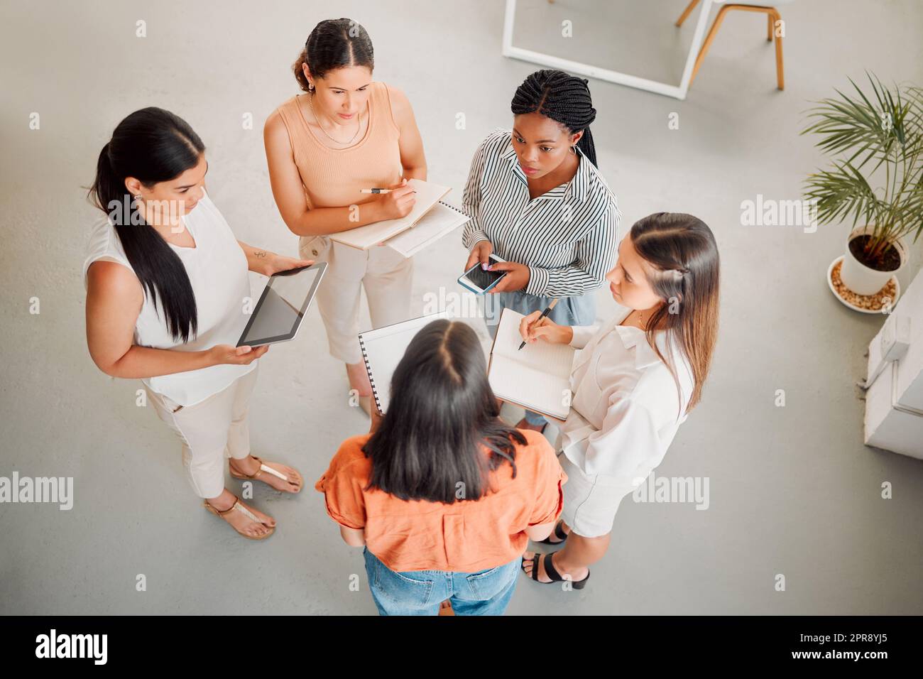Vielfältige Gruppe von fünf Geschäftsfrauen, die sich bei der Arbeit treffen. Seriöse Geschäftsleute, die sich unterhalten und planen, während sie in einem Büro von oben stehen Stockfoto