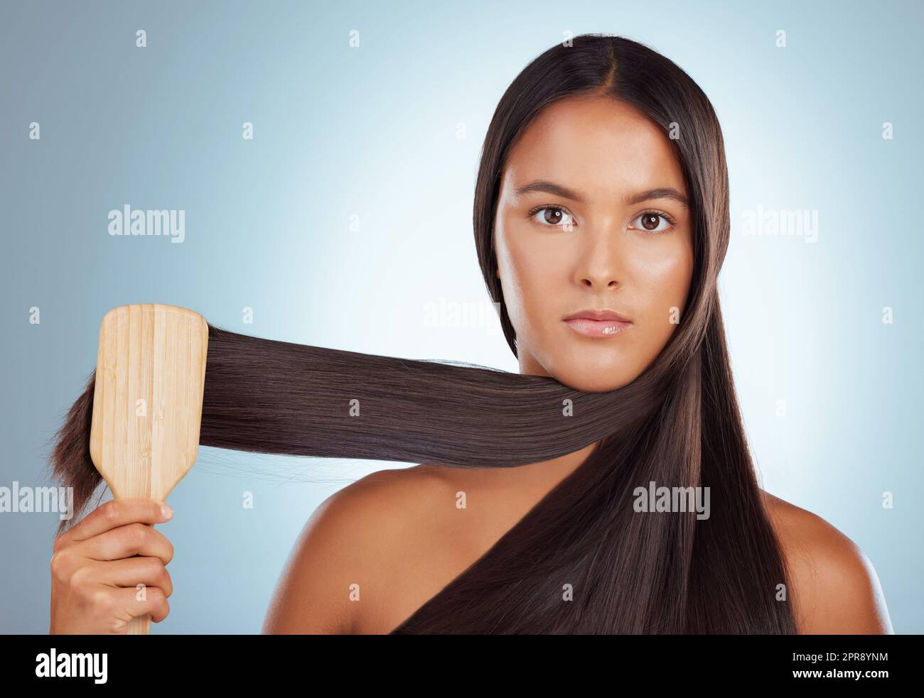 Porträt einer schönen jungen Mischrassenfrau, die ihr gesundes, kräftiges Haar vor einem grauen Studiohintergrund putzt. Hispanische Frau, die ihr Haar stöhnt Stockfoto